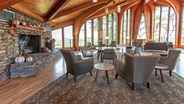 A spacious lounge with a stone fireplace, comfortable seating, and large windows offering views of the outdoors.