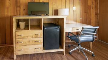 A wooden desk with a television, a lamp, a small refrigerator, and a chair.