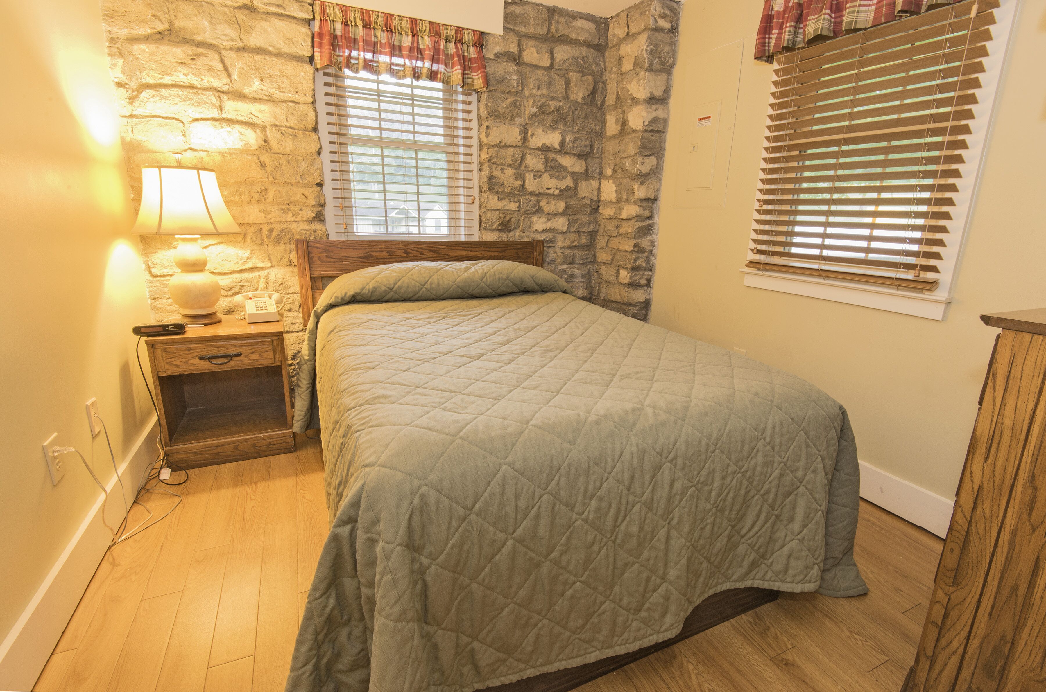 Un dormitorio con una cama, mesita de noche, lámpara y pared de piedra.