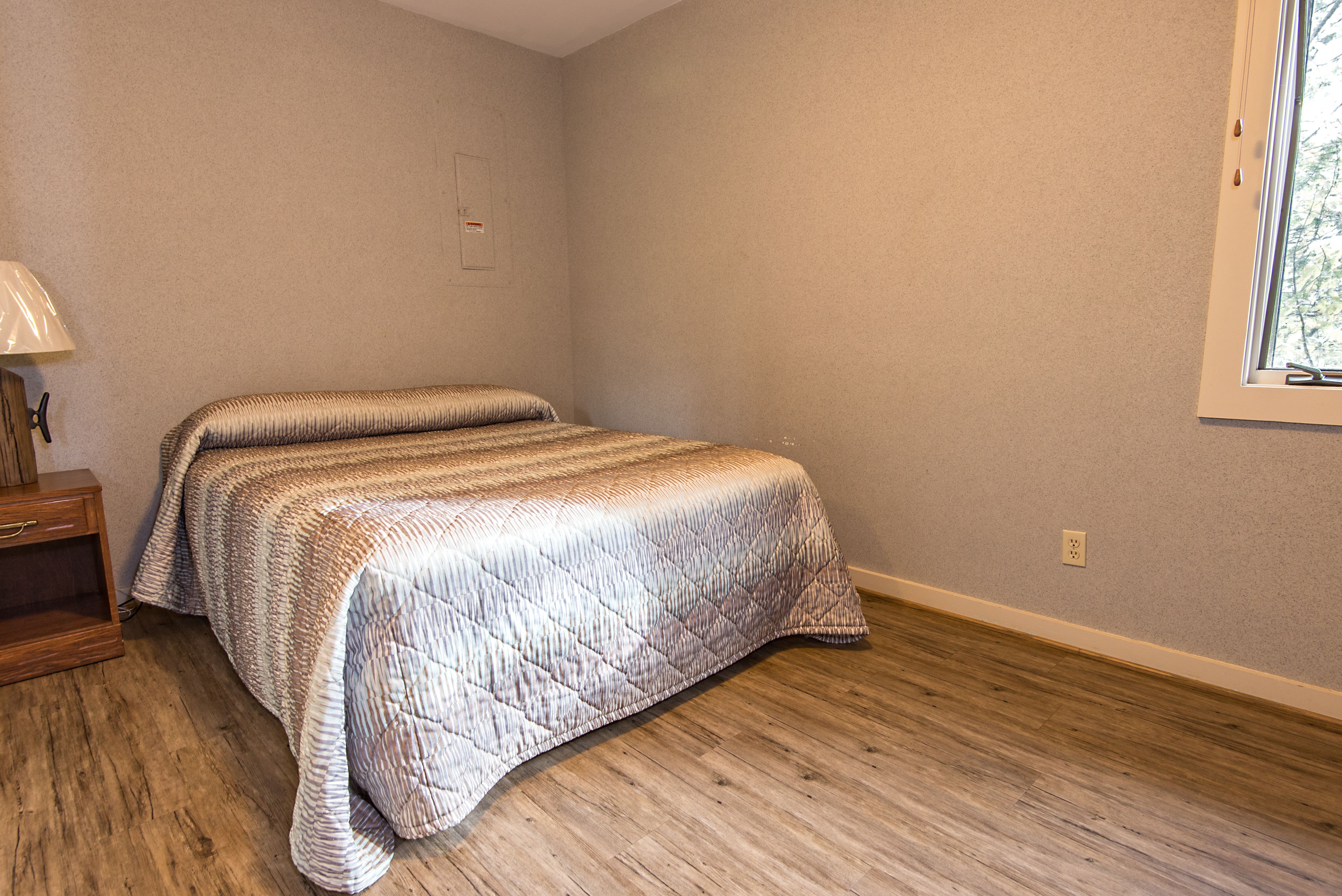 A bedroom with a bed, wooden floor, and a window.