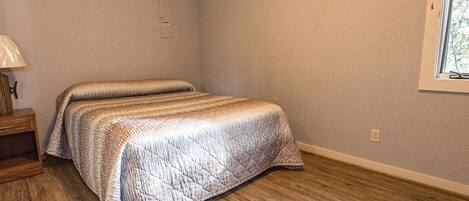 A bedroom with a bed, wooden floor, and a window.