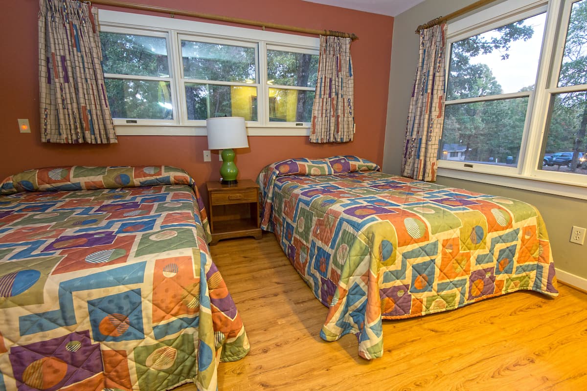 A bedroom with two beds, a nightstand, a lamp, and a window with curtains.