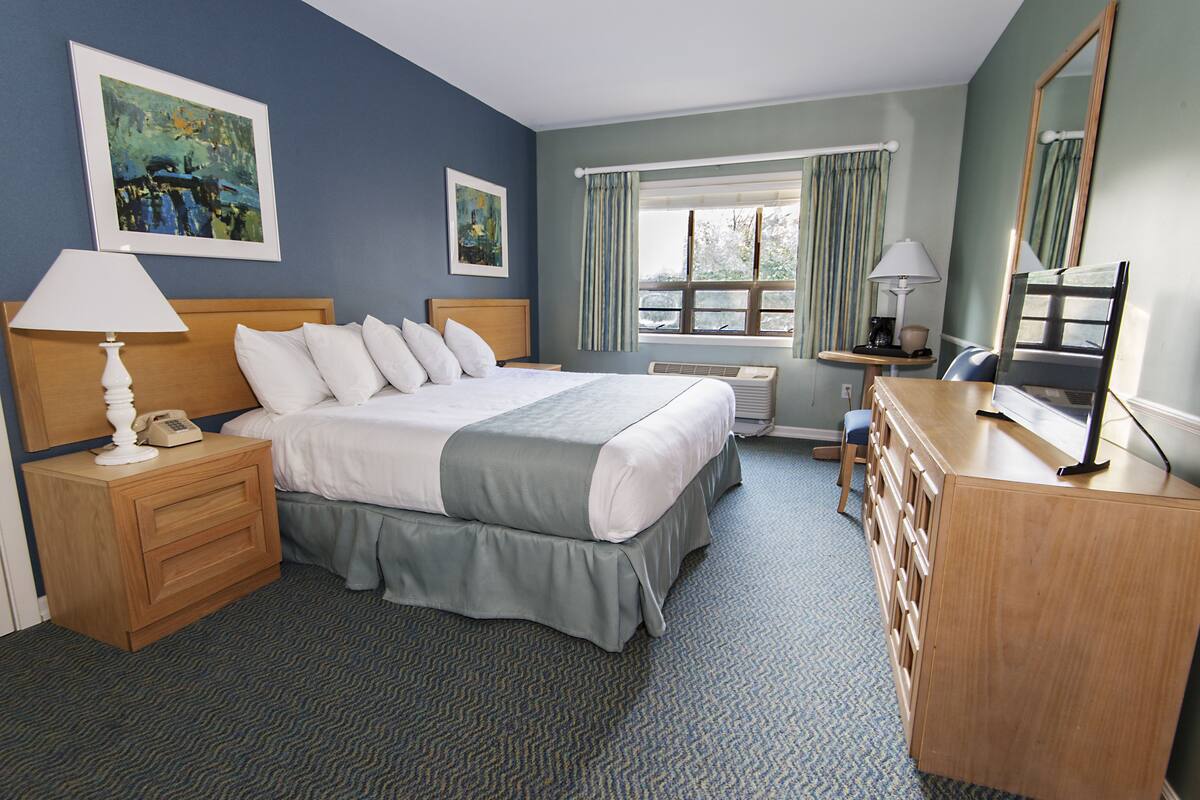A hotel room with a large bed, bedside tables, a dresser, and a window with curtains.