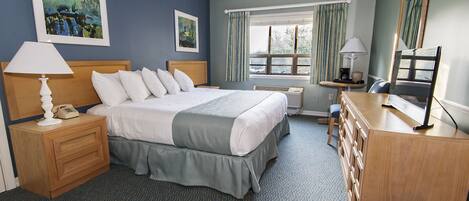 Una habitación de hotel con una cama grande, mesitas de noche, un aparador y un ventanal con cortinas.