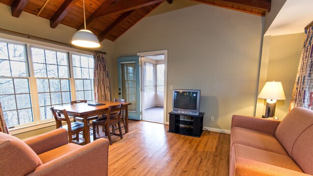 A living room with a wooden floor, a TV on a stand, a dining table with chairs, and a sofa. - Kenlake State Resort Park (Hardin)