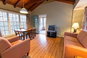 A living room with a wooden floor, a TV on a stand, a dining table with chairs, and a sofa. - Kenlake State Resort Park (Hardin)
