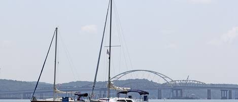 Two sailboats on calm water with a bridge in the background.