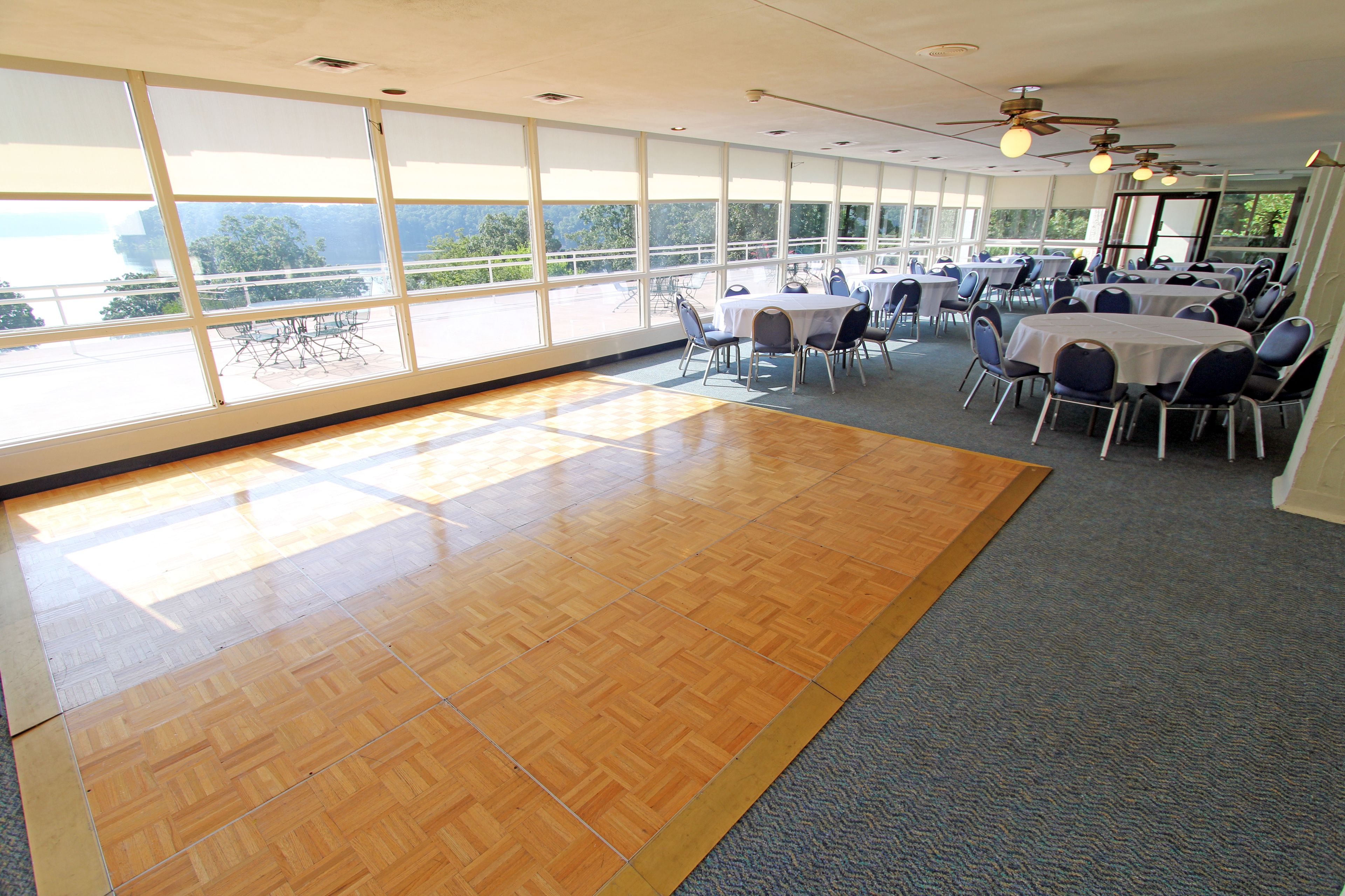 A spacious room with large windows, a wooden dance floor, and tables set up for dining.