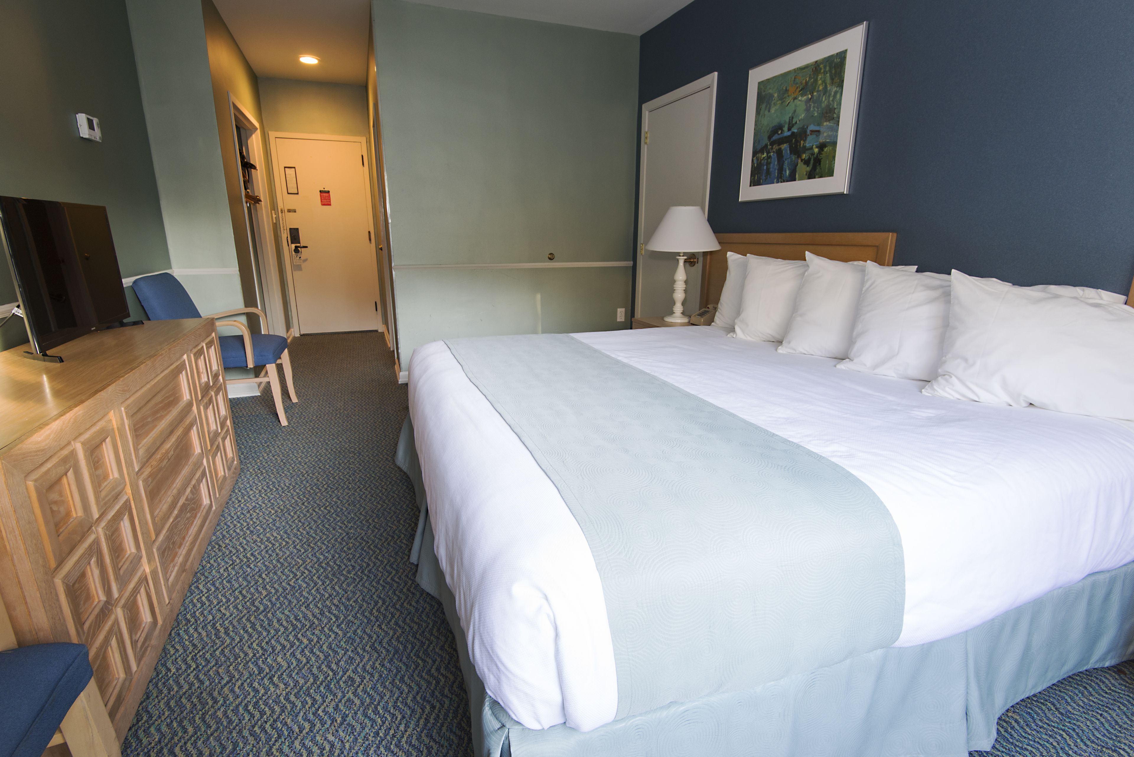 Een hotelkamer met een groot bed, een bureau met stoel, een lamp en een schilderij aan de muur.