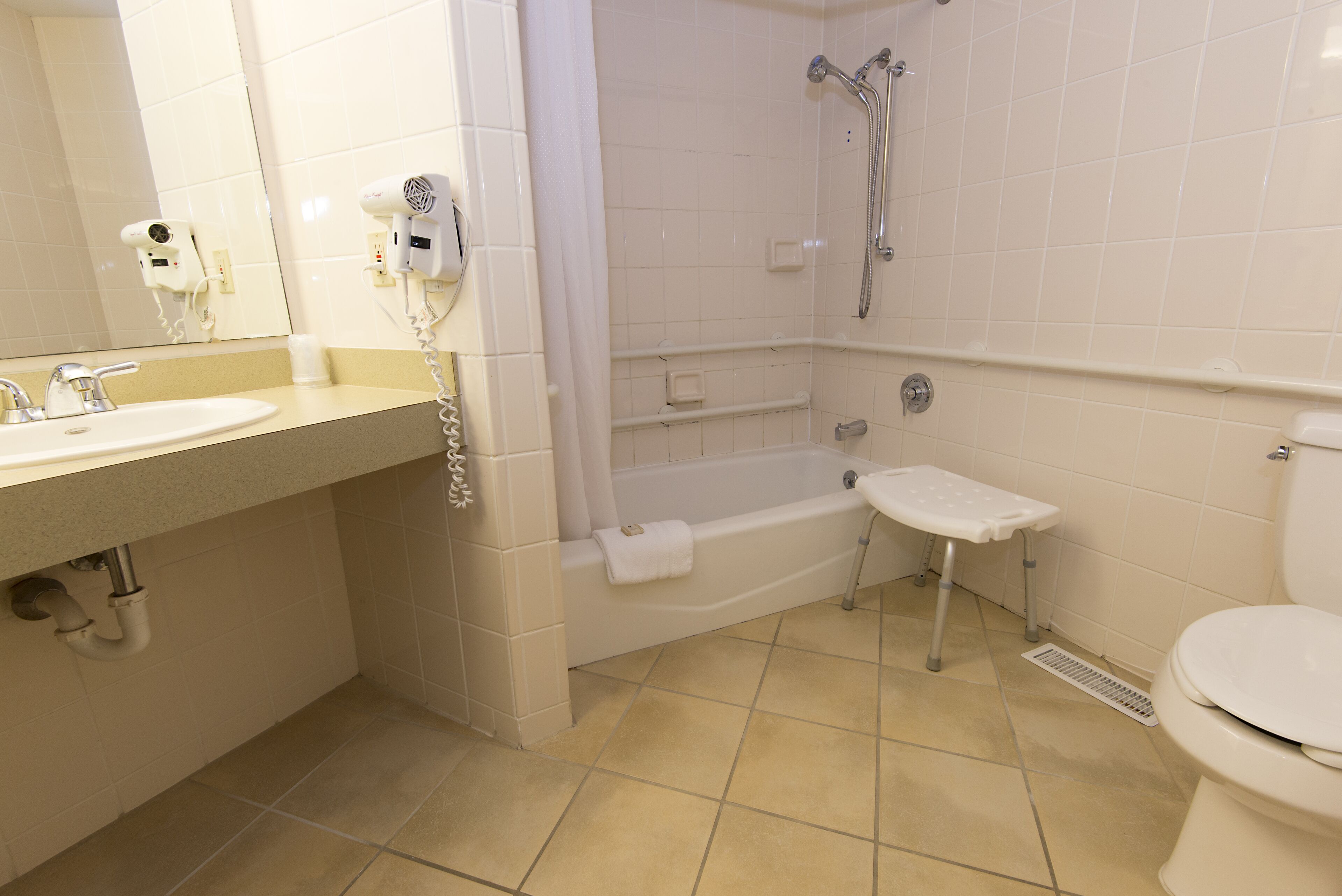 A bathroom with a sink, mirror, hair dryer, shower, and toilet.