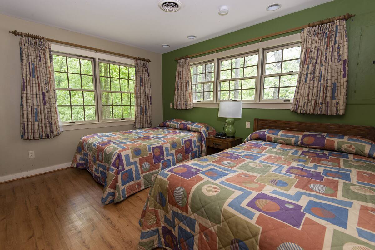 A room with two beds, large windows, and a green wall.
