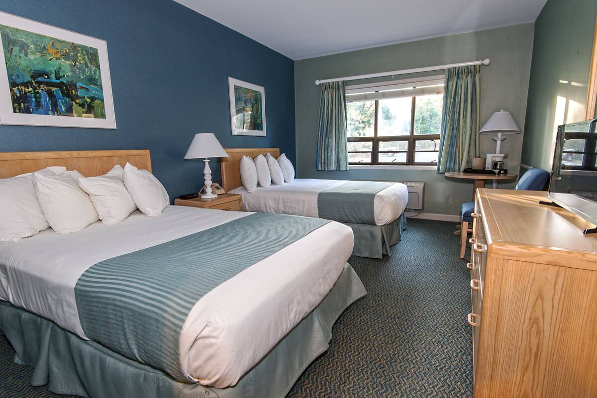 A hotel room with two beds, a desk with a lamp, a television, and artwork on the walls.