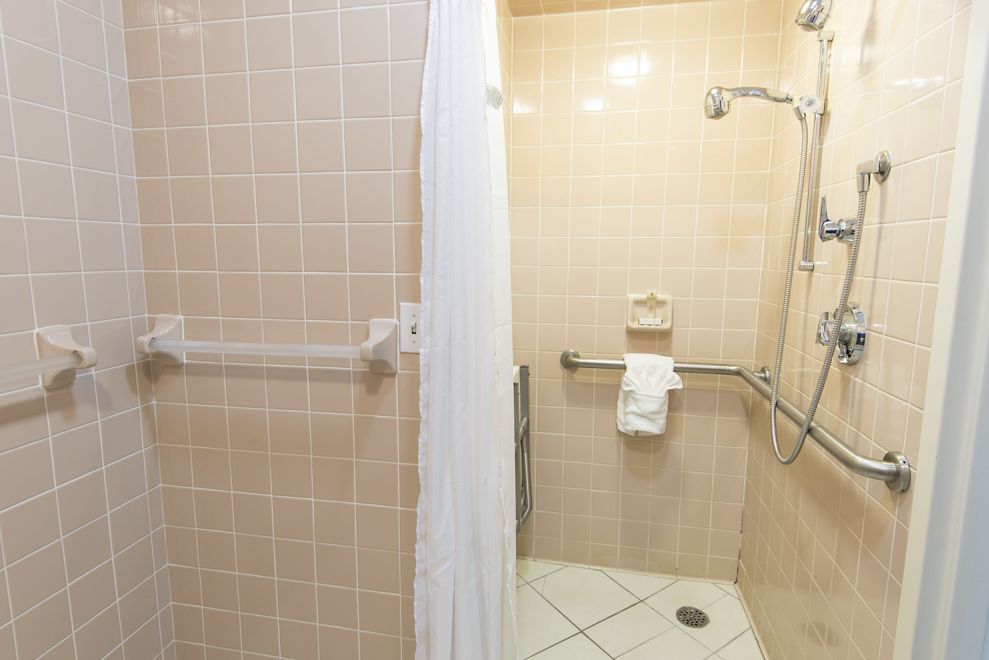 Pequeño rincón de ducha con azulejos, una barra de apoyo, una toalla blanca y un cabezal de ducha.