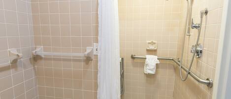 A small, tiled shower area with a grab bar, a white towel, and a showerhead.