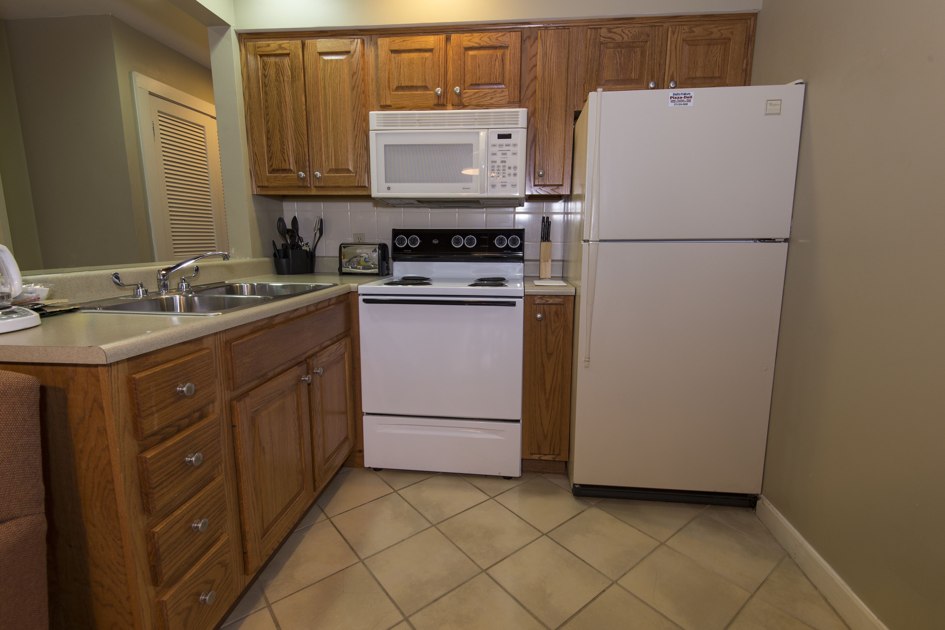 A kitchen with wooden cabinets, a white stove, a microwave, and a refrigerator.