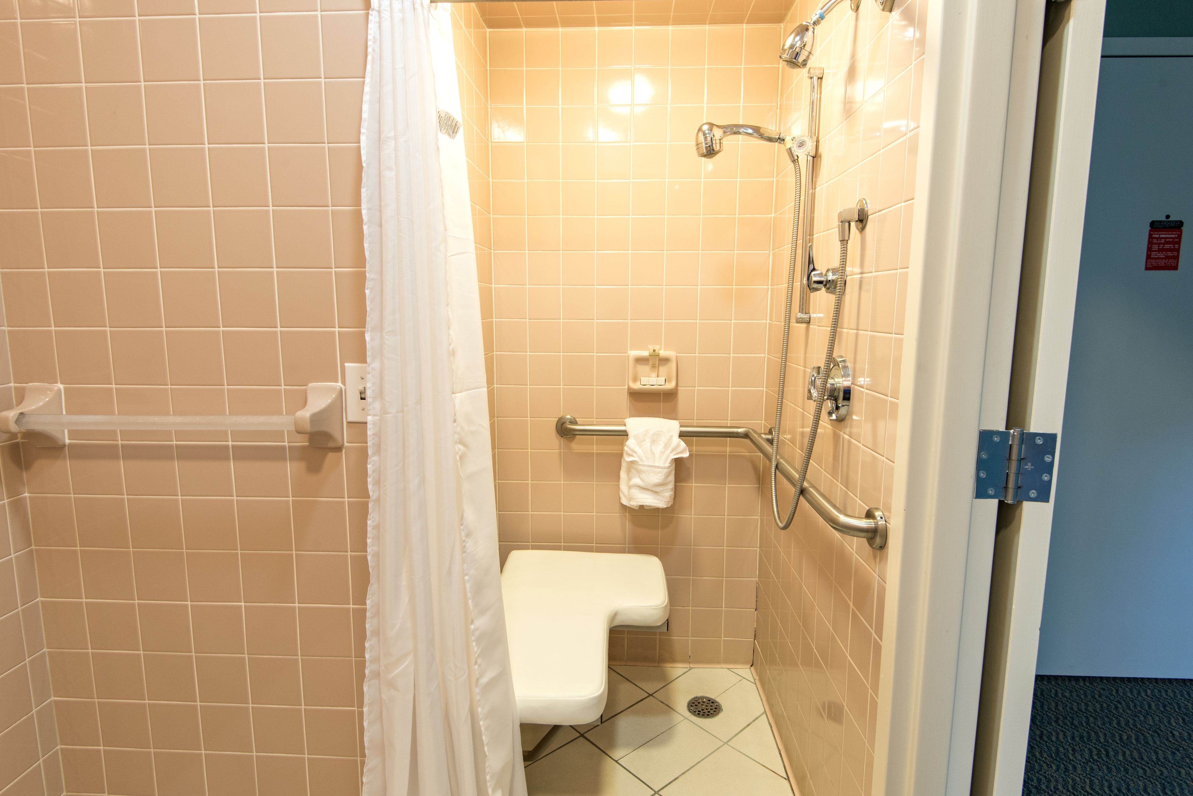 A small, tiled bathroom with a shower, a toilet, and a grab bar.