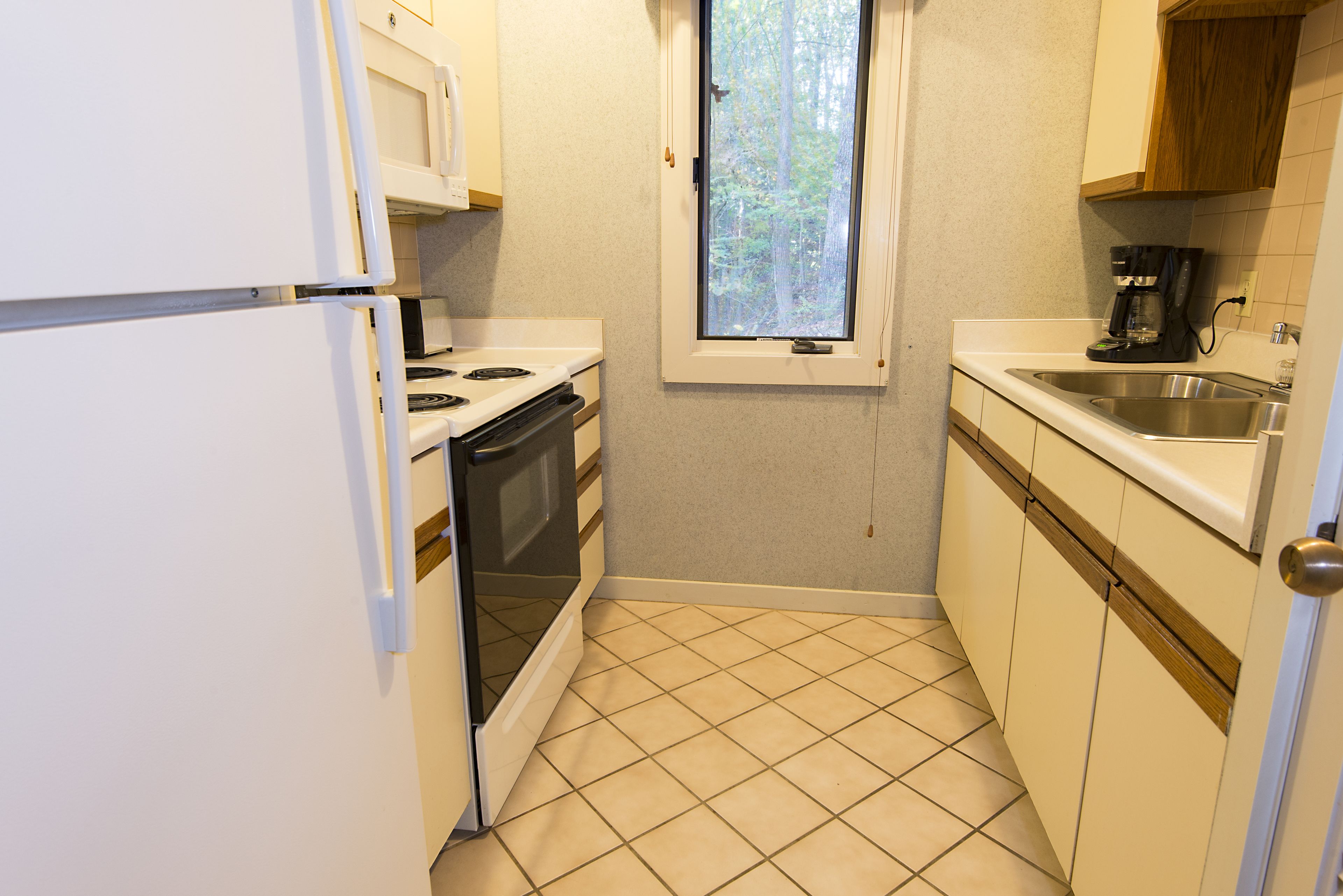A compact kitchen with a stove, oven, dishwasher, and a window providing natural light.