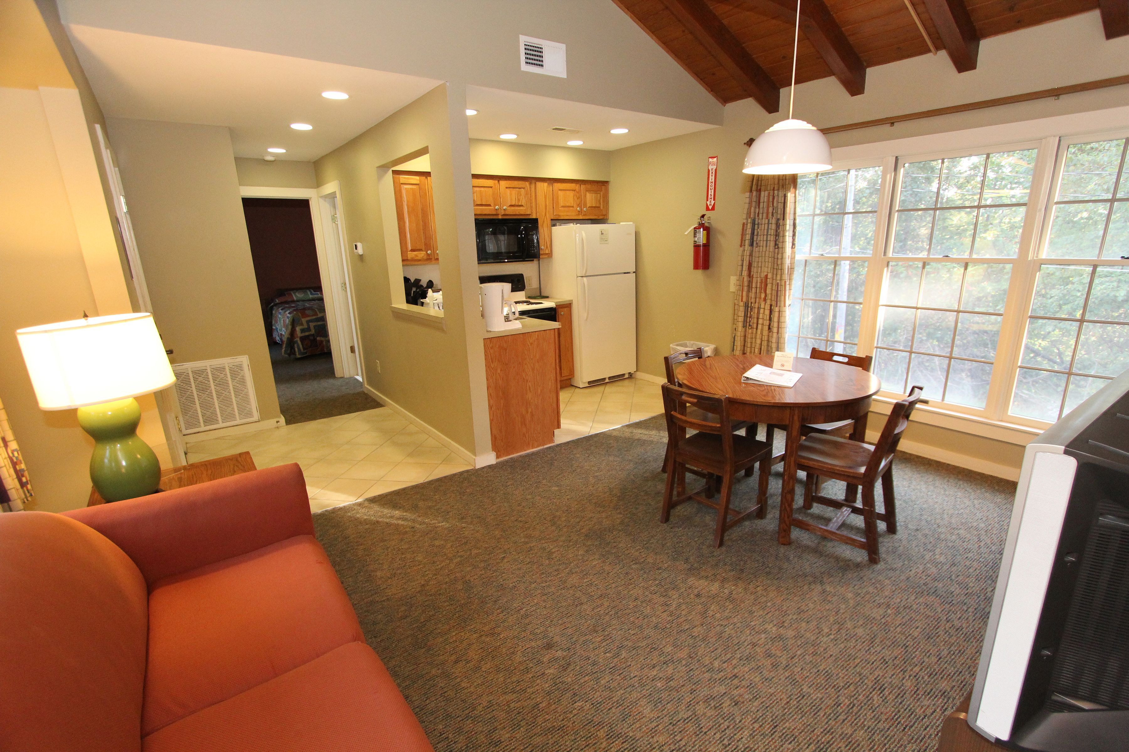 A compact living space with a dining area, kitchenette, and a large window providing natural light.