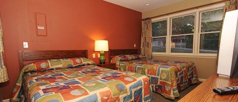 A hotel room with two beds, a desk, a lamp, and a window with curtains.