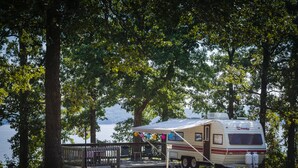 A recreational vehicle (RV) parked near a lake, surrounded by trees and a wooden deck. - Kenlake State Resort Park (Hardin)