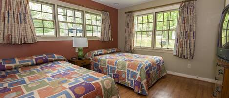 A bedroom with two beds, large windows, a nightstand with a lamp, and a dresser.