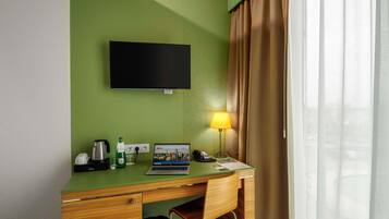 Habitación de hotel con pared verde, televisor de pantalla plana, escritorio con ordenador portátil, lámpara y cafetera.