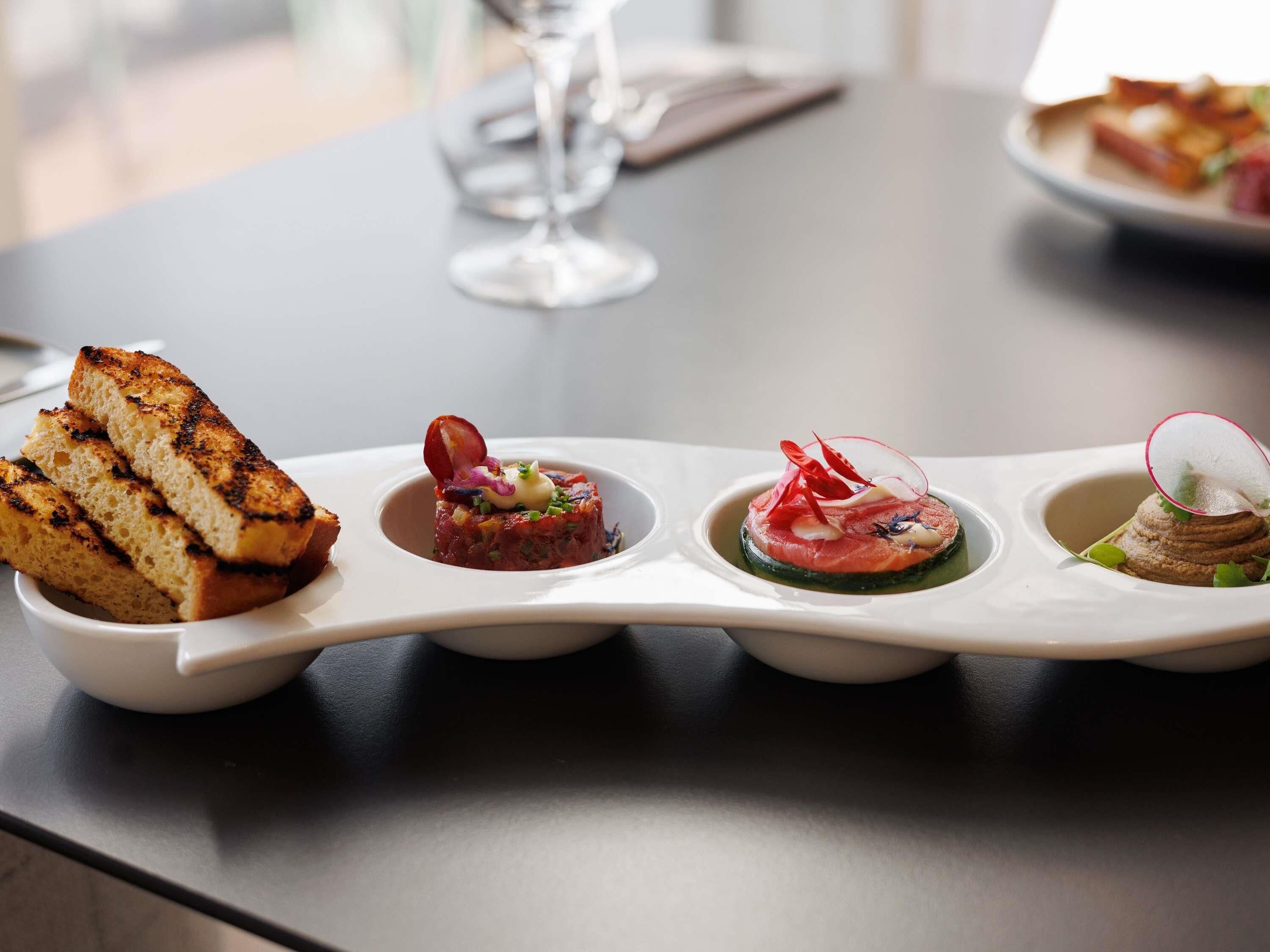 Una mesa con una variedad de platos, incluyendo pan a la parrilla, una tartaleta y dos fuentes pequeñas con distintos alimentos.