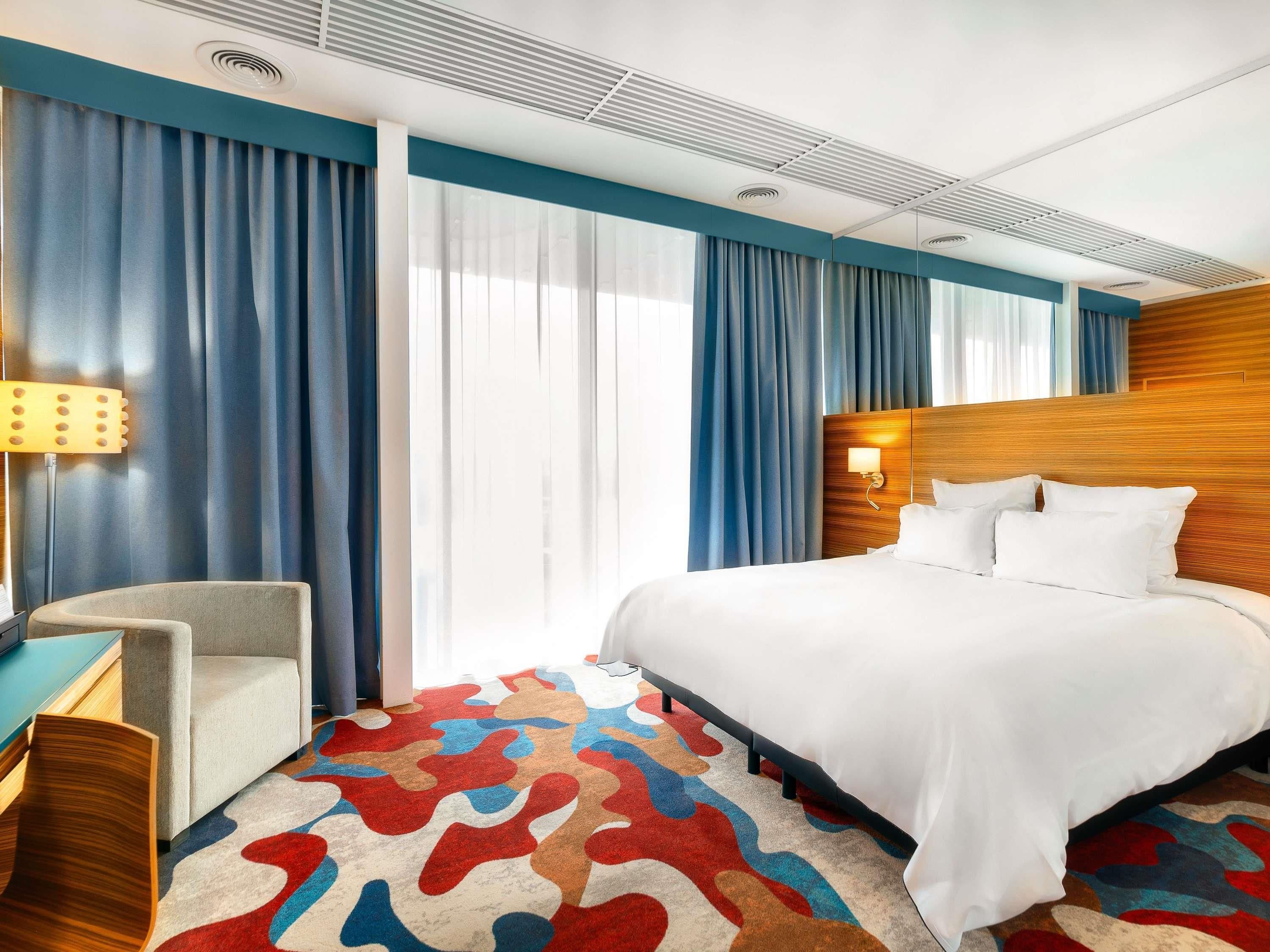 Habitación de hotel con cama, escritorio, silla y alfombra colorida.