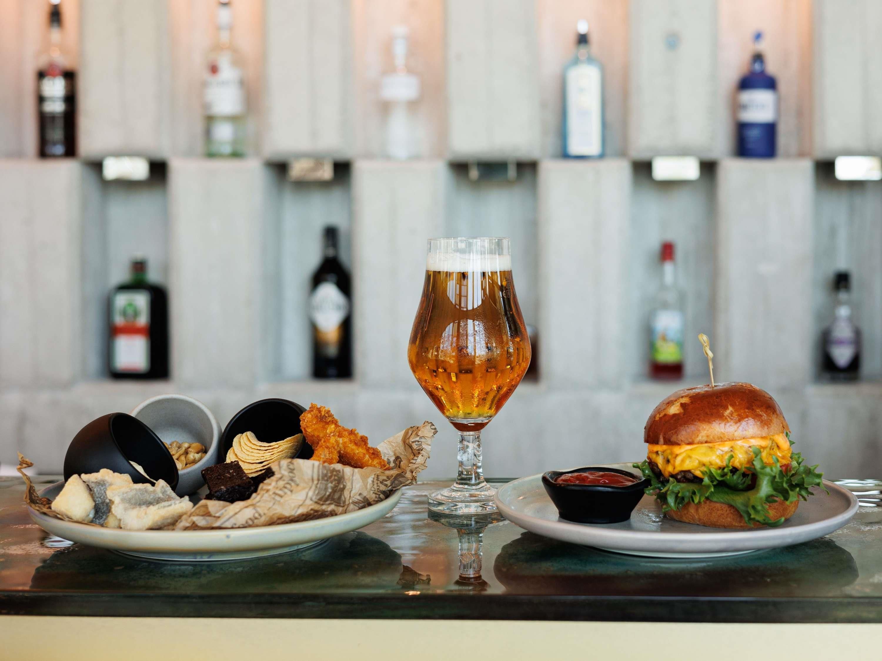 A bar setting with a glass of beer, a burger, fried items, and a bottle of wine.