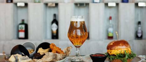 A bar setting with a glass of beer, a burger, fried items, and a bottle of wine.