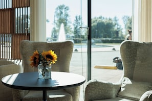 A room with a round table and two armchairs, a vase with sunflowers, and a view of a fountain and trees outside. - Mercure Tallinn (Tallinn)