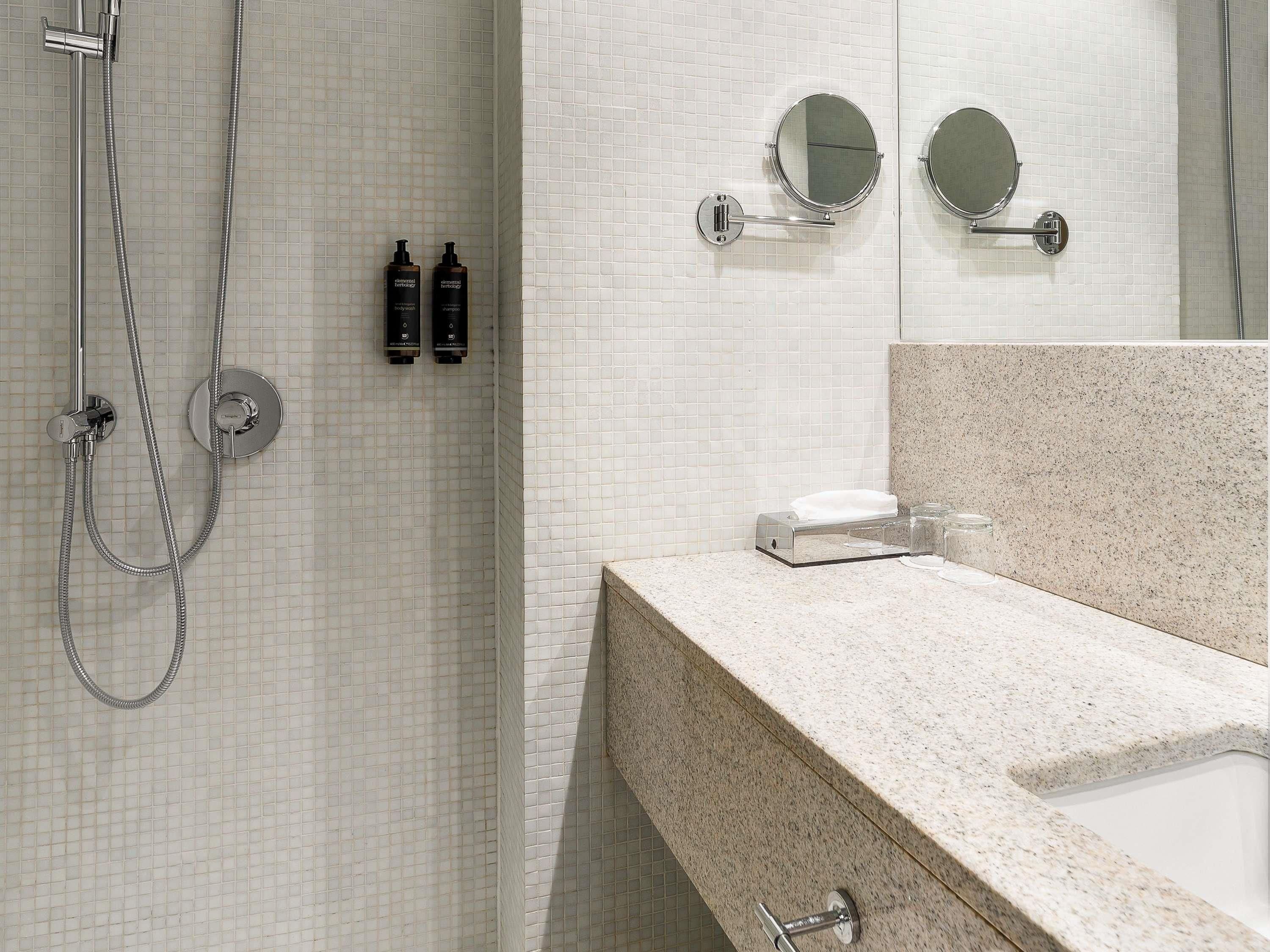 A bathroom with a shower, two mirrors, a sink, and two bottles of shampoo.