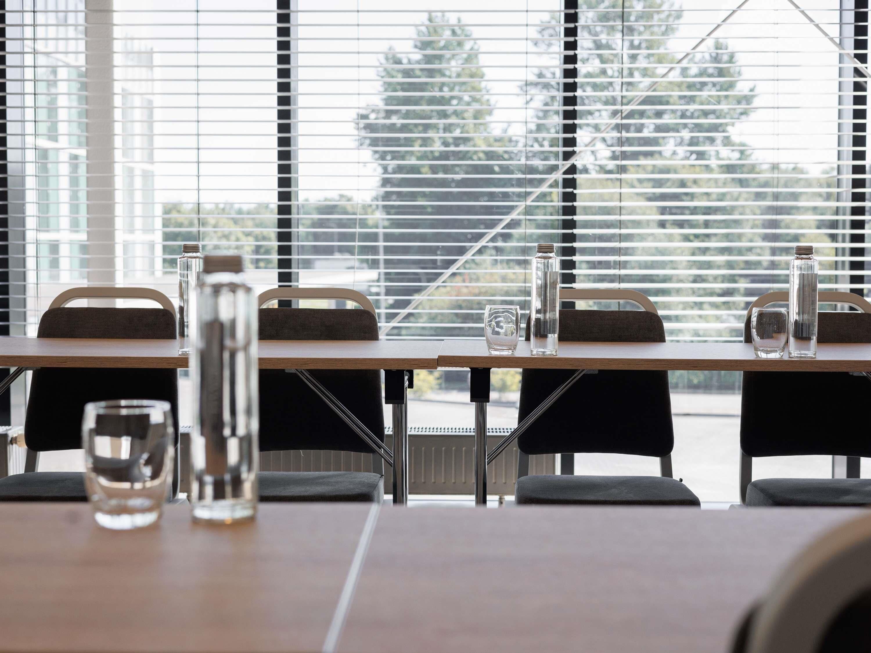A modern dining area with tables, chairs, and a view of trees through large windows.