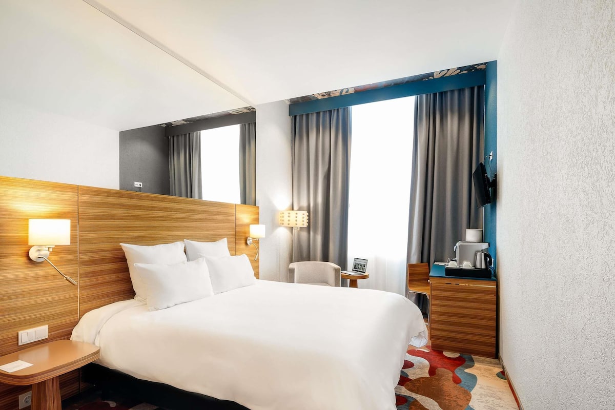 Une chambre d’hôtel avec un grand lit, des tables de chevet, un bureau, une chaise, une télévision et une fenêtre avec des rideaux.