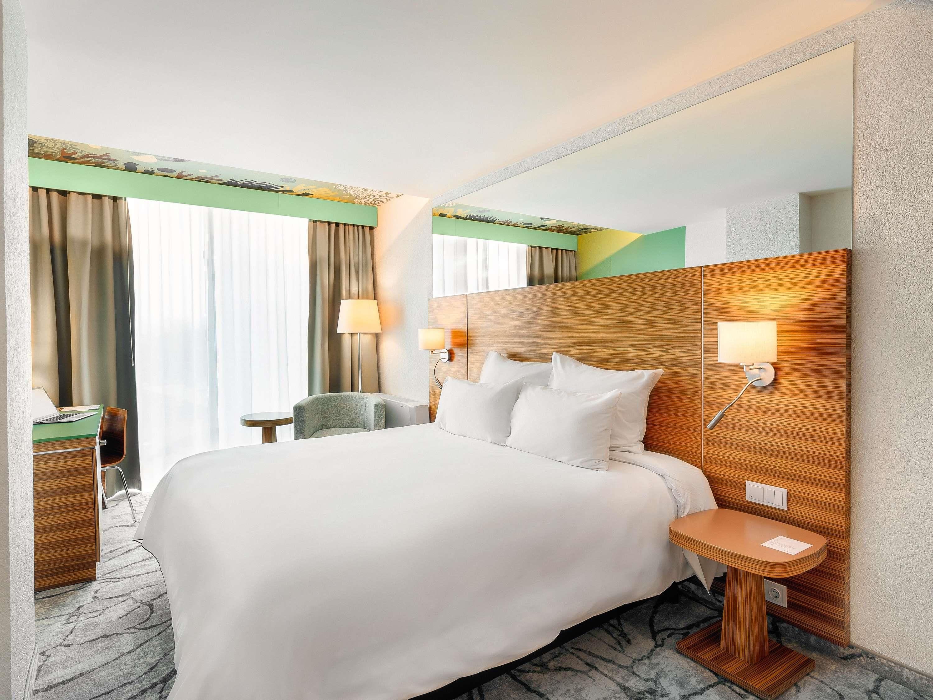 Habitación de hotel con una cama grande, un escritorio, una silla, una lámpara y un espejo.