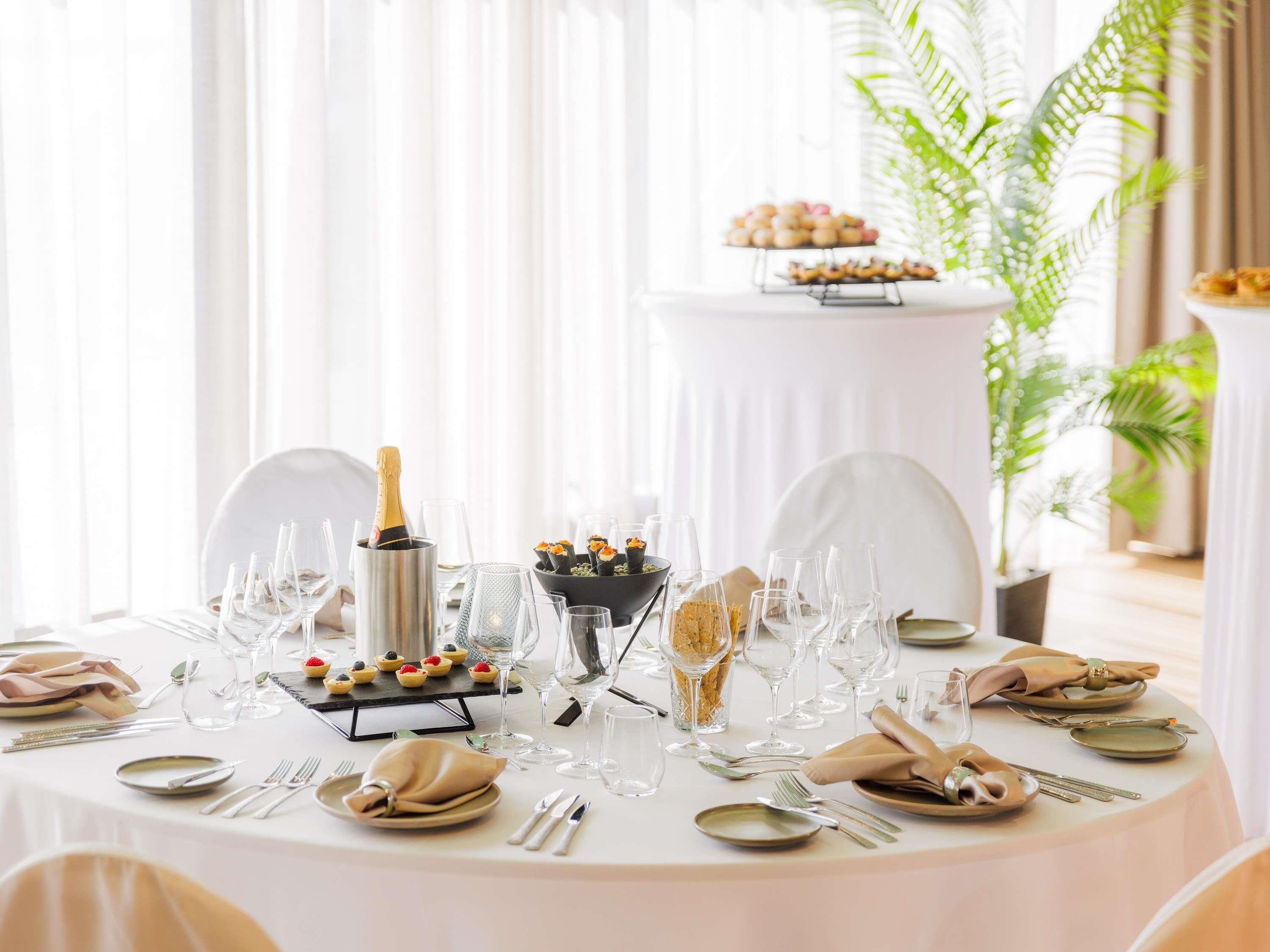Un tavolo da pranzo rotondo apparecchiato per un evento formale, con una bottiglia di champagne, bicchieri e un buffet di dolci.