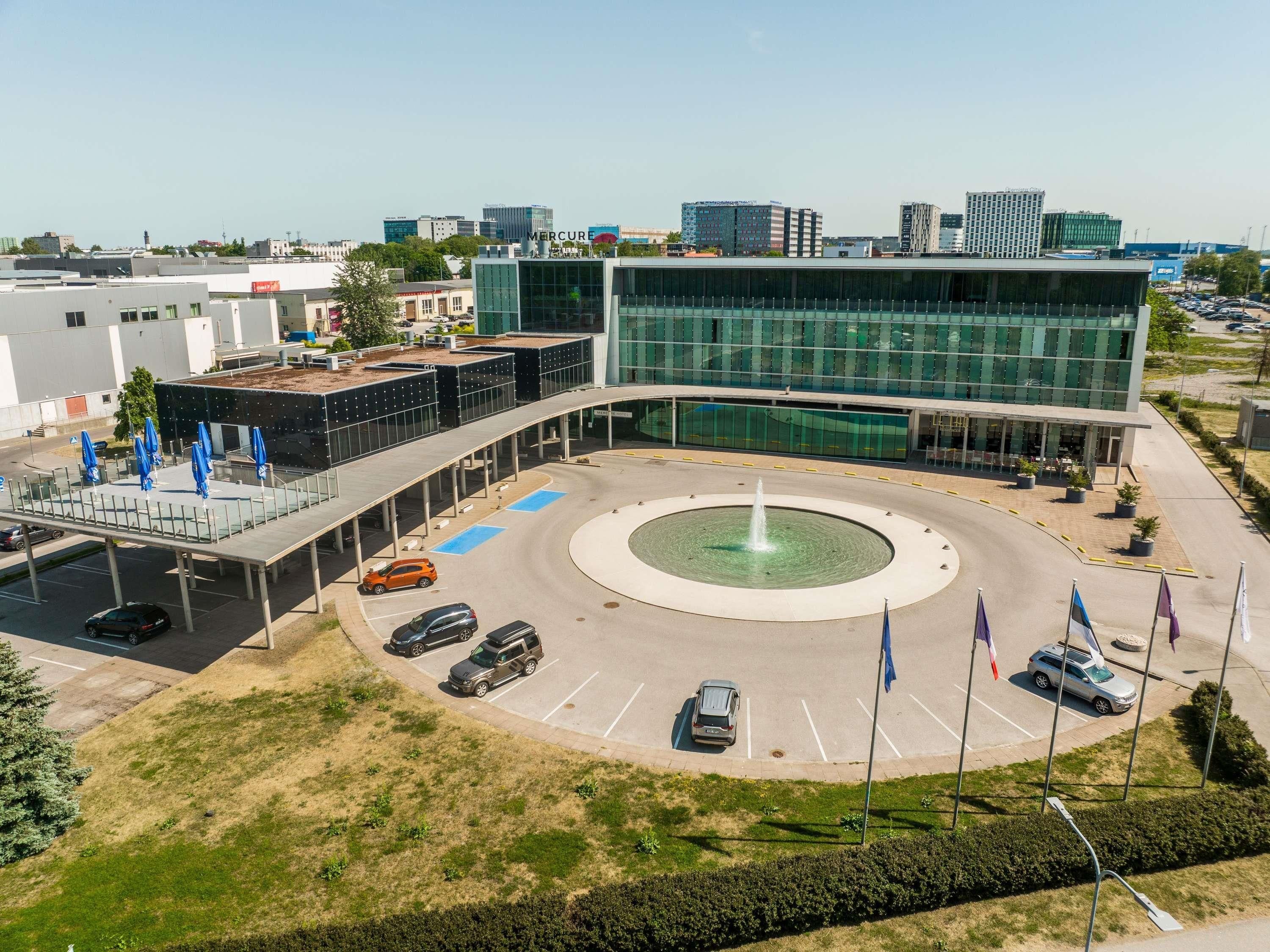 A modern building with a central fountain, parking spaces, and a covered walkway.