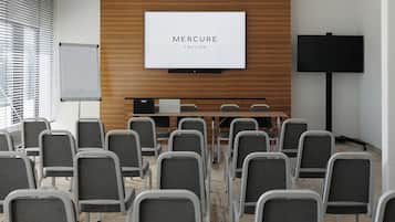 A conference room with rows of chairs facing a large screen displaying 'MERCURE TALLINN'.