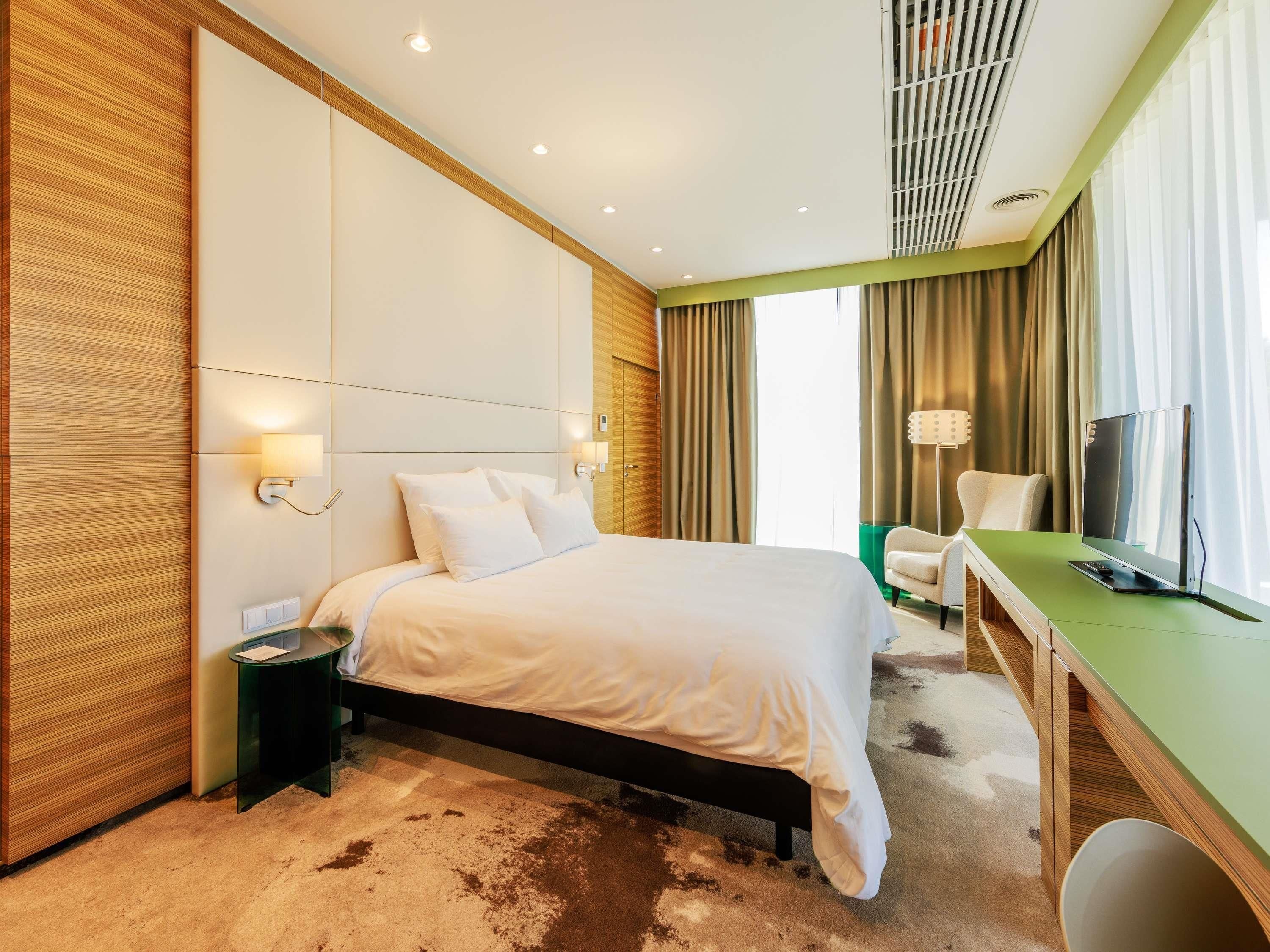 Ein Hotelzimmer mit Bett, Nachttisch, Lampe, Fernseher und Schreibtisch mit Stuhl.