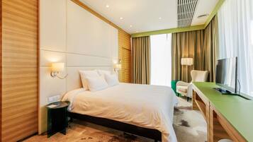 Ein Hotelzimmer mit Bett, Nachttisch, Lampe, Fernseher und Schreibtisch mit Stuhl.