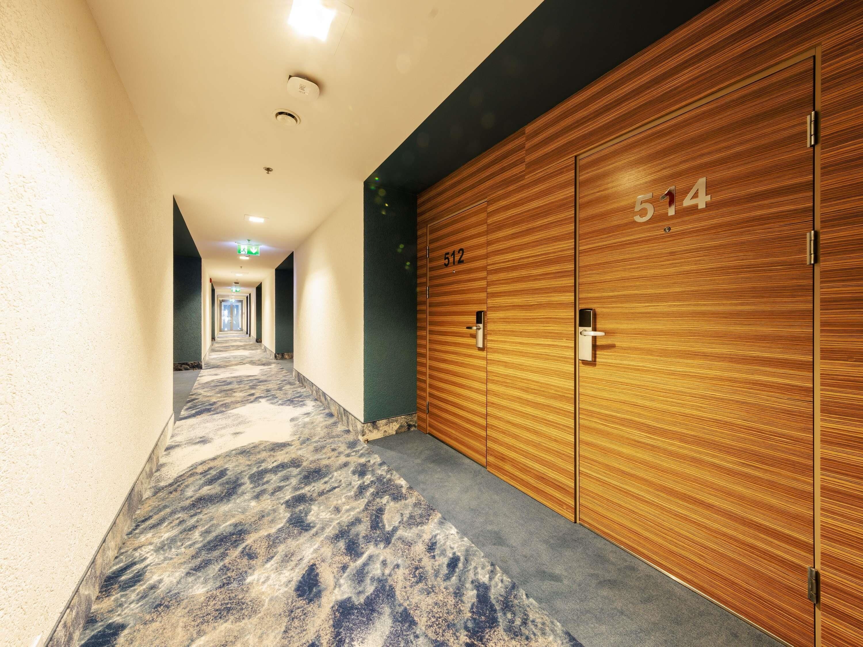 Un pasillo de hotel con taquillas de madera, numeradas 512 y 514, piso alfombrado e iluminación empotrada en el techo.