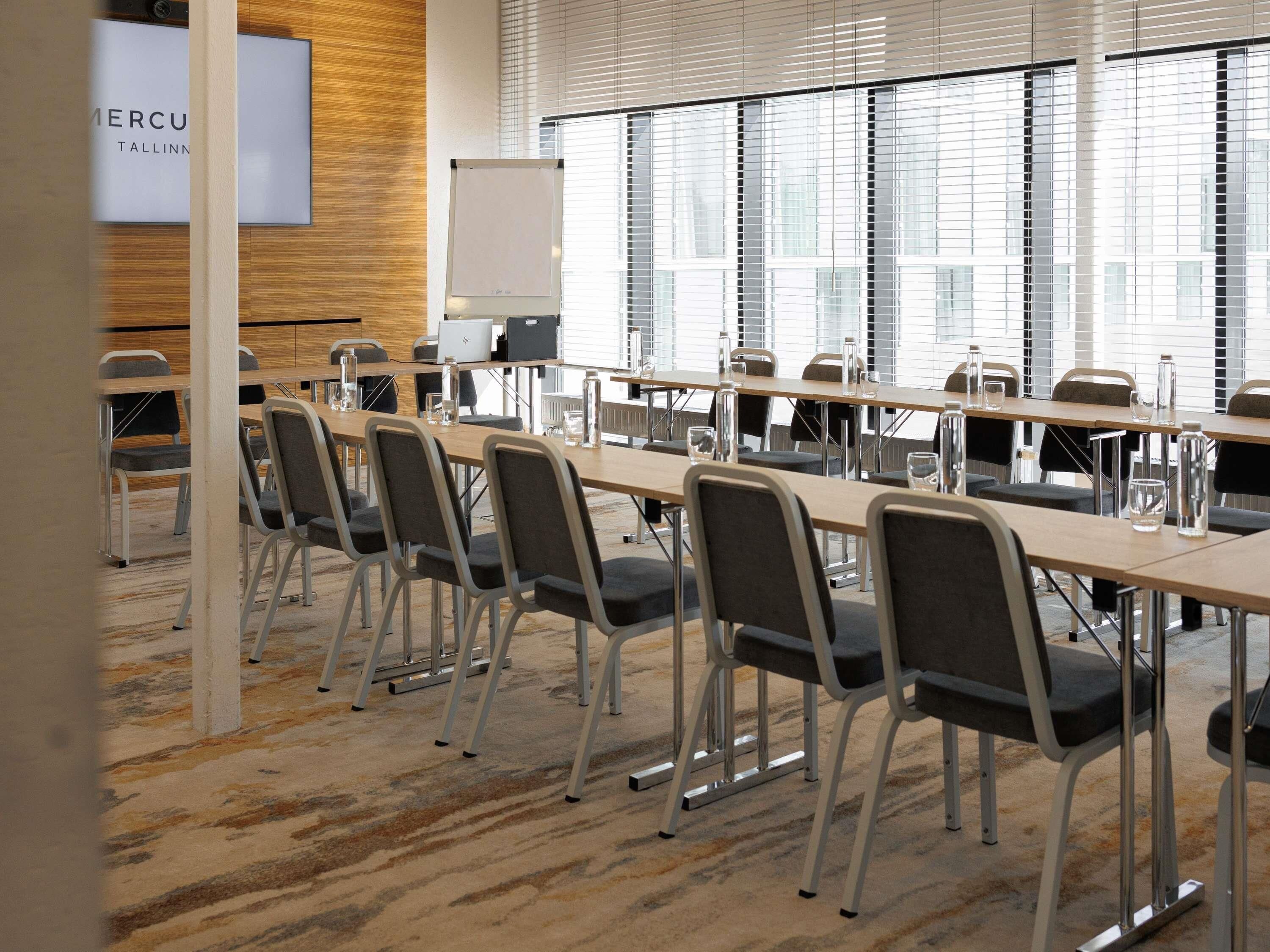 A conference room with long tables, chairs, a whiteboard, and a laptop.