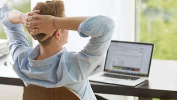Una persona sentada en un escritorio usando una computadora portátil, vistiendo una camisa azul claro.