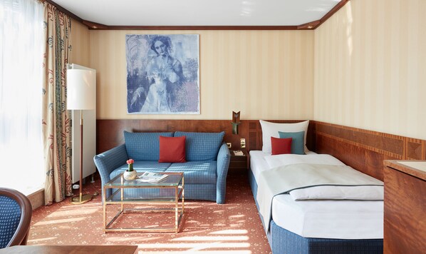 Una habitación de hotel con un sofá, una cama, una mesa de centro de vidrio y un cuadro en la pared.