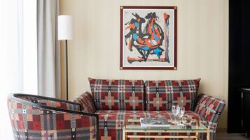 A living room with a patterned sofa, a glass coffee table, and a framed abstract painting on the wall.