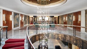 En rymlig entréhall med en storslagen kristallkrona, marmorgolv och en röd matta som täcker trappan.