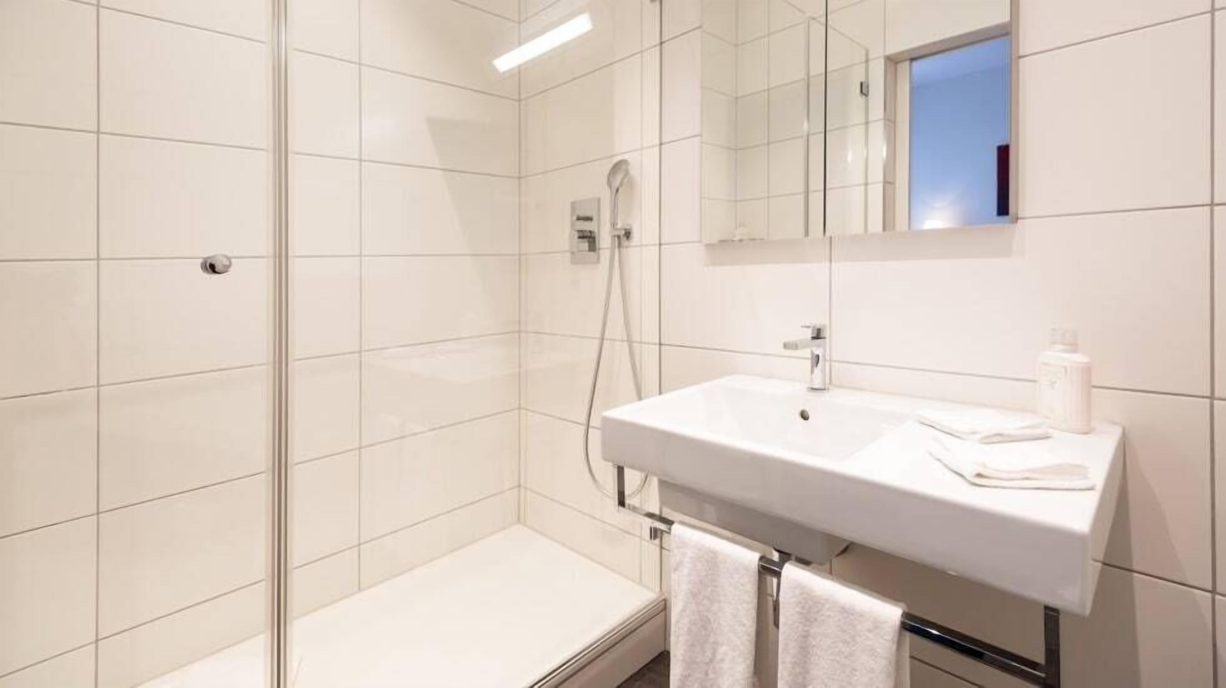 A modern bathroom with a glass-enclosed shower, a white sink, and a mirror above it.