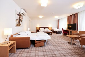Quarto de hotel com cama, escrivaninha, televisão, poltrona e luminária.