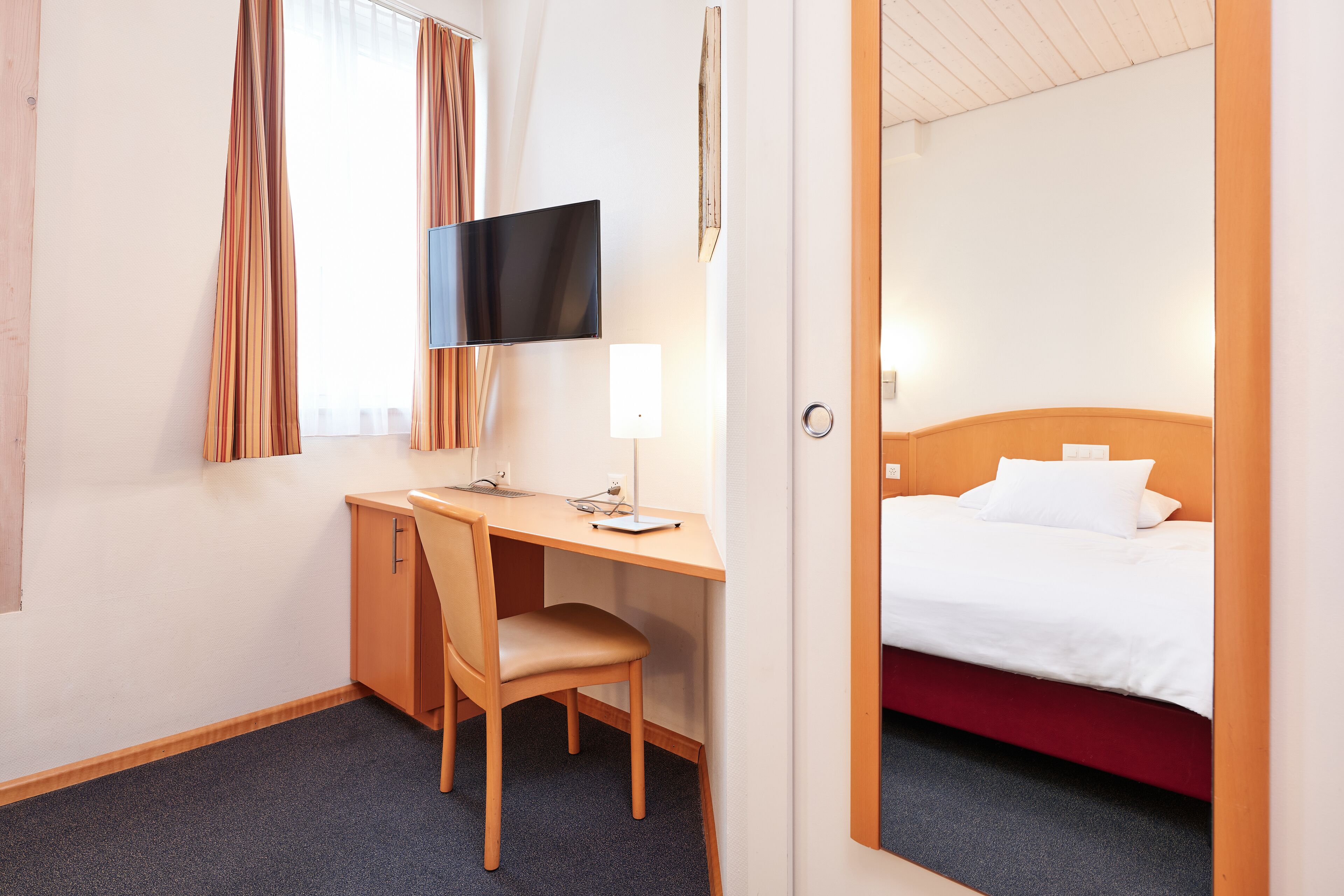 Una habitación de hotel con escritorio, silla, televisión y cama con ropa de cama blanca.