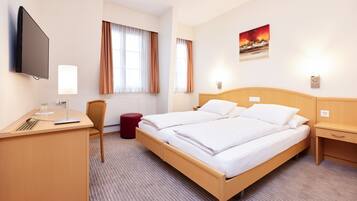 Una camera d'albergo con un letto, una scrivania, una sedia, una televisione e un quadro appeso al muro.